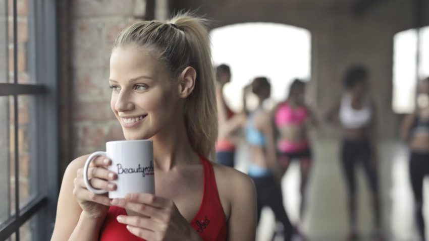 Woman in activewear enjoying a coffee break indoors at a gym in Budapest.
